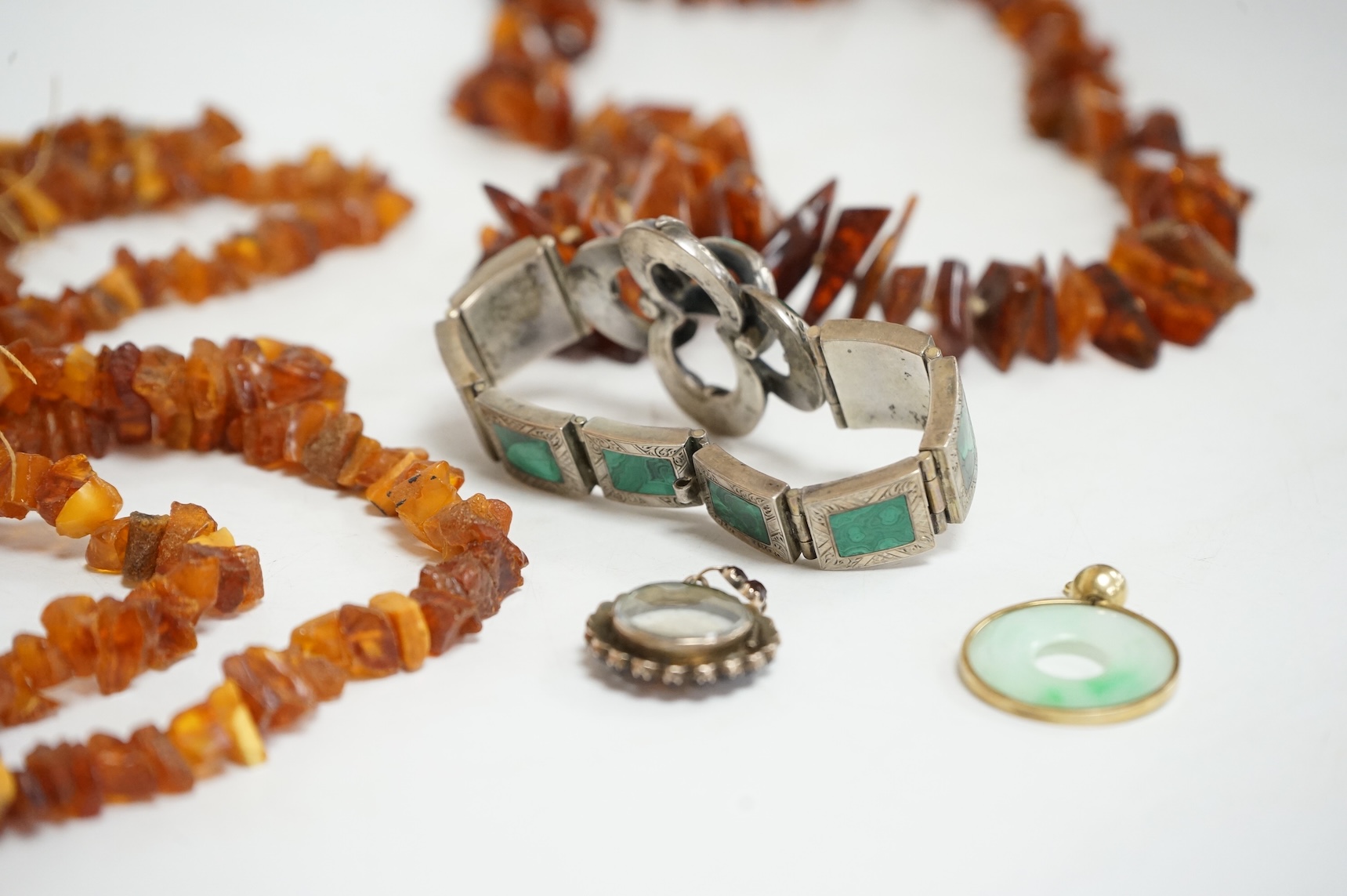 An early to mid 20th century engraved white metal and malachite set 'knot' bracelet, together with a Victorian garnet and enamel portrait pendant, a mounted jadeite disc pendant and two amber necklaces.